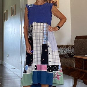 Può includere: Un abito patchwork con un top blu e una gonna realizzata con vari modelli di tessuto, tra cui quadri, pois e stampe floreali. L'abito ha un aspetto unico e fatto a mano. La persona indossa sandali con plateau neri.