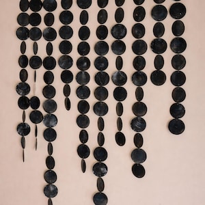 Puede incluir: Decoración mural que presenta numerosos elementos circulares y ovalados de color azul oscuro suspendidos de una barra de madera. La disposición crea un efecto en cascada, similar a una cortina, añadiendo un elemento textural único a la pared.