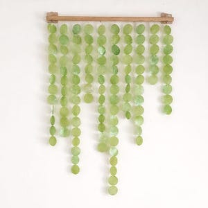 Puede incluir: Dos sillas de madera con cojines marrones y cojines decorativos con un estampado de hojas blancas y burdeos. Arriba, un adorno de pared de cuentas verdes y circulares cuelga de una barra de madera. Una pintura enmarcada está arriba.