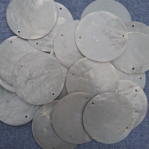 May include: A pile of grey, circular discs, each with a small hole near the edge. The discs have a slightly textured surface. The background is a blue fabric. These could be decorative elements.