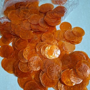 May include: A large collection of translucent, circular orange shell sequins, each featuring a small pre-drilled hole for attachment. These flat, round discs exhibit a natural, iridescent texture and are partially contained within a clear plastic bag.