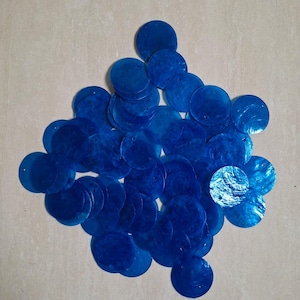 Peut inclure: Une collection de sequins circulaires en coquillage bleu avec une finition irisée naturelle. Chaque pièce plate et ronde présente un petit trou central pour la fixation, affichant une teinte bleue vive et profonde avec des variations de texture.