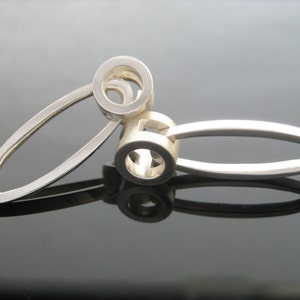 May include: Two silver rings interlocked, one is a simple oval shape, the other is a circle with a smaller circle cut out of it.