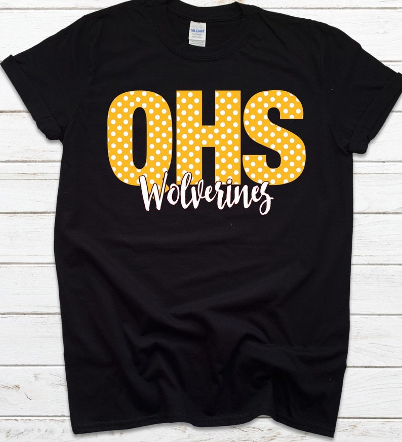 May include: Black t-shirt with the letters "OHS" in yellow with white polka dots. Below the letters, the word "Wolverines" is written in a white script font. The shirt is made of a soft material.