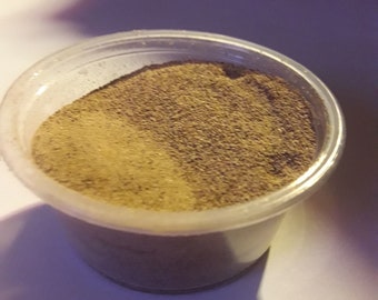 May include: A small plastic container filled with a light brown powder. The powder is a mixture of two shades of brown, with a lighter brown on the top and a darker brown on the bottom.