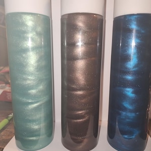 May include: Three clear glass bottles with white lids filled with shimmering liquid. The liquid in the bottles is teal, brown, and blue.