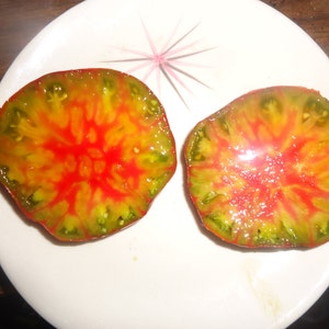 Op de afbeelding: Twee helften van een tomaat, doormidden gesneden, tonen de binnenkant. De tomaat is fel rood en geel met groene strepen. De tomaat ligt op een wit bord.
