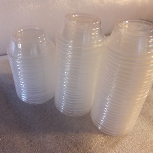 Può includere: Una pila di bicchieri di plastica trasparente, con tre bicchieri singoli nella parte anteriore. I bicchieri sono impilati ordinatamente e pronti per l'uso.