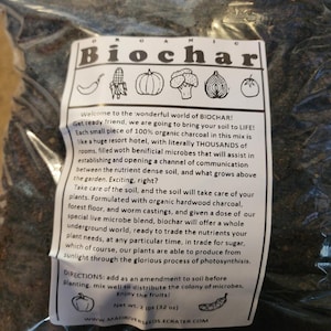 May include: A bag of black biochar soil amendment with a white label that says "Biochar" and includes a description of the product. The label also includes a list of vegetables and the text "Net Wt. 2 lbs (32 oz)" and "www.madriverseeds.ecrater.com".