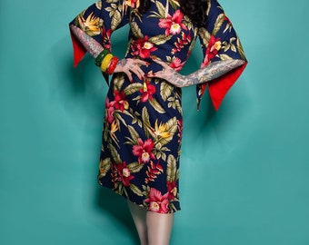 May include: A navy blue dress with a vibrant floral pattern of red and yellow flowers and green leaves. The dress features wide sleeves with red cuffs and is paired with red sandals. The model is wearing bracelets and earrings.
