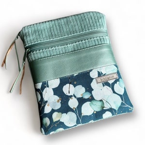 Könnte beinhalten: Eine türkisfarbene Reißverschlusstasche mit einem grünen Cord-Oberteil, einem grünen Lederpanel und einem türkisfarbenen Stoffboden mit weißem Blumenmuster und goldenen Akzenten. Die Tasche hat ein kleines braunes Lederetikett mit dem Wort "kodanin" darauf.