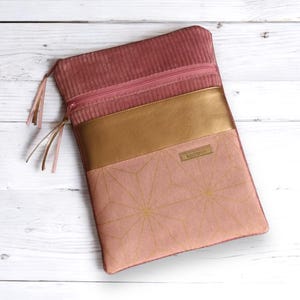 Könnte beinhalten: Eine Laptop-Hülle aus rosa Cord mit einem goldenen Reißverschluss und einem goldenen Lederakzent. Die Hülle hat ein geometrisches Muster mit goldenen Akzenten und das Wort "Leotard" ist auf dem Lederakzent aufgedruckt.