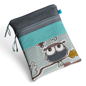 Könnte beinhalten: Eine graue und blaue Reißverschlusstasche mit einem niedlichen Eulen-Design. Die Eule ist braun, grau und weiß mit großen Augen und sitzt auf einem Ast mit Blättern. Die Tasche hat ein türkisfarbenes Stoffpanel und ein graues Stoffpanel.