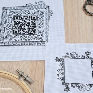 May include: Two white Aida cloth cross stitch patterns. The first pattern features a black and white QR code surrounded by a black floral design. The second pattern features a black floral design with a blank square in the center.