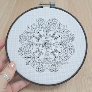 May include: Black and white embroidery hoop with a floral mandala design. The design features intricate details of leaves, flowers, and geometric patterns.