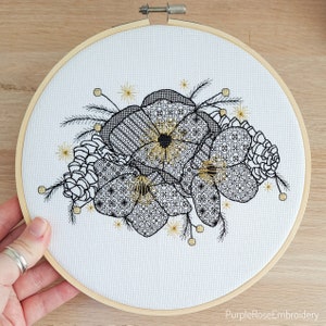 May include: An embroidery hoop with a floral design. The design features black and white flowers with intricate patterns, accented with gold details. The embroidery is on white fabric, and the hoop is made of wood. The text "PurpleRoseEmbroidery" is at the bottom.