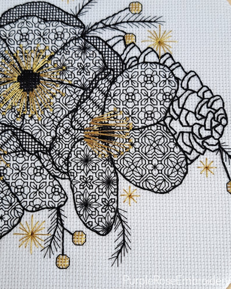 May include: Close-up of a cross-stitch embroidery featuring a floral design. The artwork showcases black and gold thread on a white background. The floral elements have intricate geometric patterns, with gold accents and starburst details.