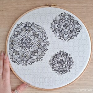 May include: A white embroidery hoop with three black and white mandala designs. The hoop is on a wooden surface.