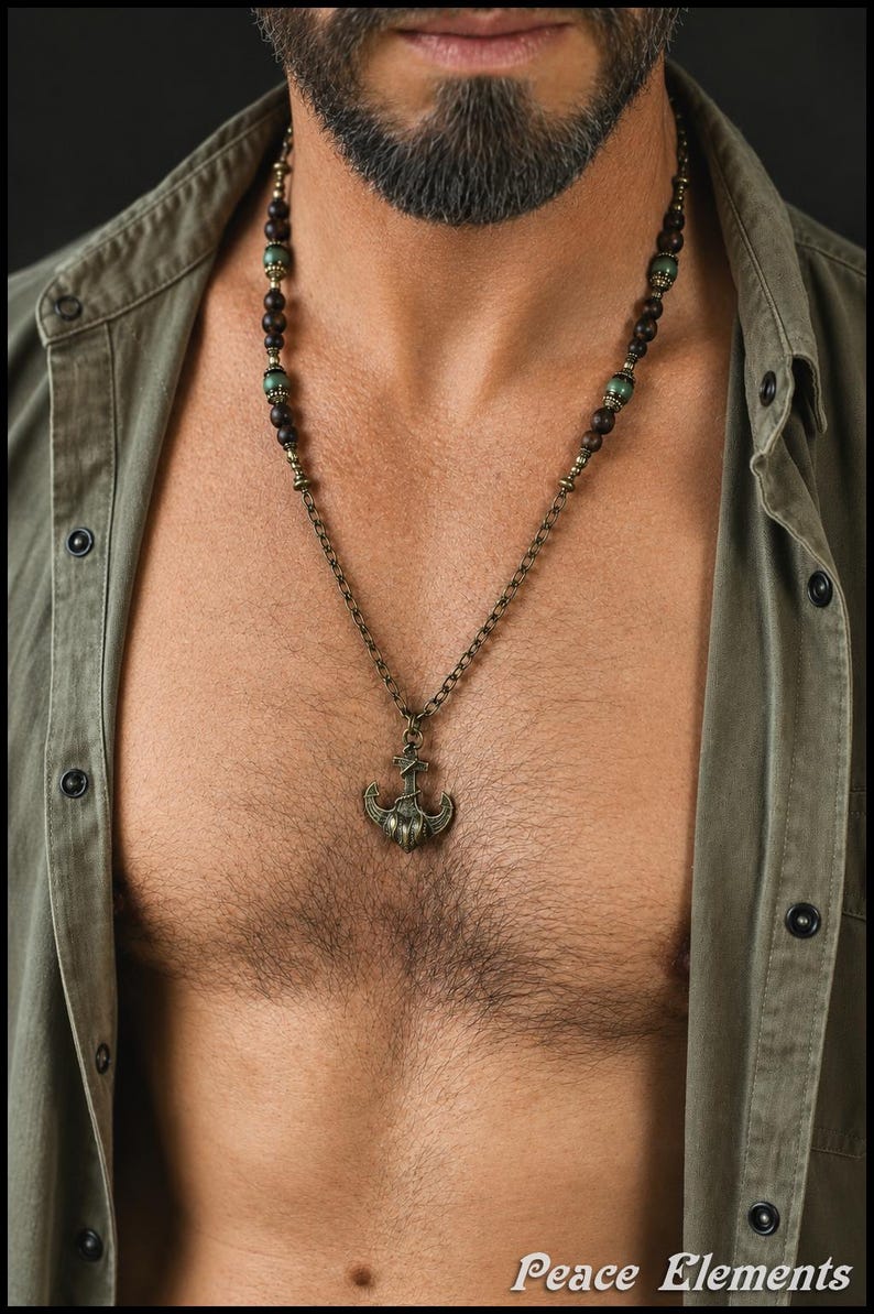 May include: A necklace featuring a bronze-toned anchor pendant suspended from a chain. The upper portion of the necklace consists of dark brown wooden beads interspersed with smaller, metallic green beads and bronze-colored spacers.