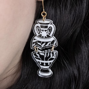 May include: A pair of black and white acrylic earrings shaped like a broken vase. The earrings are dangling from gold hooks.