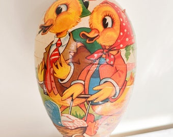 May include: A vintage Easter egg decoration with a wooden base. The egg is decorated with a colorful illustration of two ducks pushing a baby carriage.