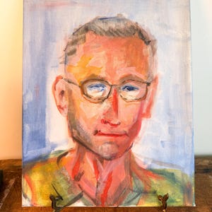 May include: An oil painting on canvas depicting a portrait of a person wearing glasses. The artwork features expressive brushstrokes in shades of blue, red, orange, and green against a light blue background, capturing facial features with visible texture.