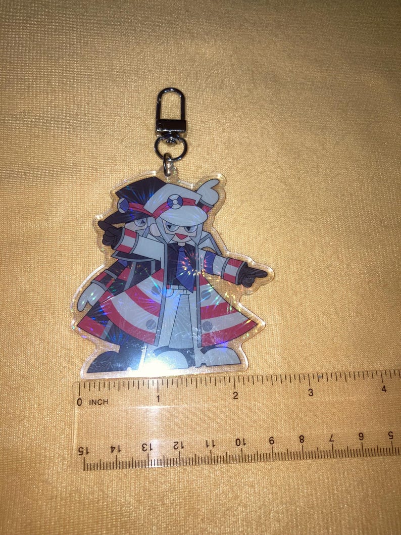 Puede incluir: Llavero acr&iacute;lico transparente con un personaje de dibujos animados con un abrigo con detalles en rojo, blanco y azul. El llavero tiene un cierre plateado. El personaje mide unos 5 cm de largo.