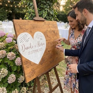 Può includere: Un cartello in legno per il libro degli ospiti di nozze su un cavalletto. Il cartello presenta un design a forma di cuore con i nomi "Davide e Ilaria" e la data "20 SETTEMBRE 2025". Gli ospiti firmano il cartello con un pennarello.