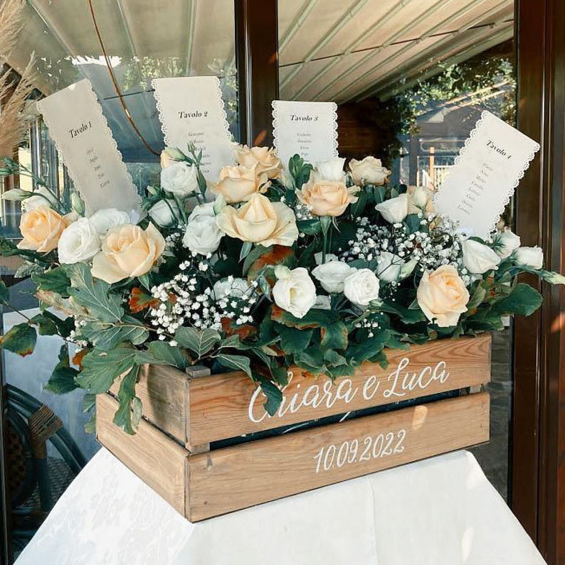 May include: A wooden crate decorated with white flowers and greenery. The crate is labeled with the names "Chiara e Luca" and the date "10.09.2022".