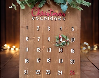 Può includere: Calendario natalizio a conto alla rovescia in legno con la scritta "Christmas" in rosso. I numeri da 1 a 25 sono visualizzati in bianco, con una piccola ghirlanda sul numero 9. Il calendario è decorato con verde e pigne.