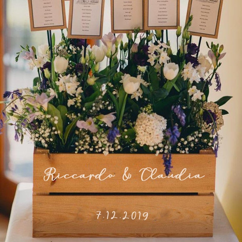 May include: A wooden crate with white flowers and greenery. The crate is decorated with the names "Riccardo & Claudia" and the date "7.12.2019".