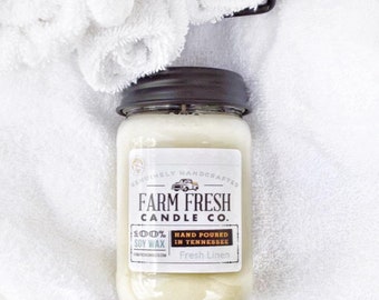 Peut inclure: Une bougie en pot avec un couvercle noir et une étiquette blanche. L'étiquette indique "Farm Fresh Candle Co." et "Fresh Linen". La bougie est coulée à la main dans le Tennessee et fabriquée avec 100% de cire de soja. La bougie est posée sur une serviette blanche.