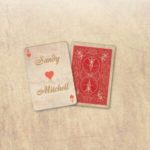 Peut inclure: Deux cartes &agrave; jouer sur un fond textur&eacute;. L'une est l'As de c&oelig;ur, personnalis&eacute;e avec les noms "Sandy" et "Mitchell" et un c&oelig;ur rouge. L'autre carte montre le dos rouge d'une carte &agrave; jouer.