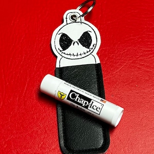 May include: A black leather keychain with a white embroidered Jack Skellington face and a ChapStick lip balm attached.