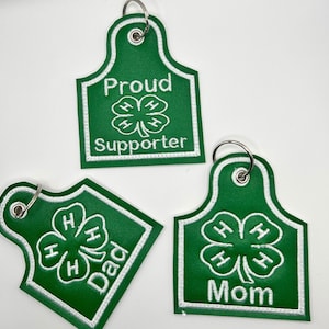 May include: Three green keychains with white embroidered 4-H clover designs. One keychain says "Proud Supporter", another says "Dad", and the third says "Mom".