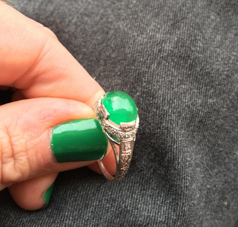 May include: A silver ring with a large, oval-shaped emerald green gemstone set in a delicate, ornate design.