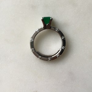 May include: A silver ring with a green gemstone and small diamonds around the band.