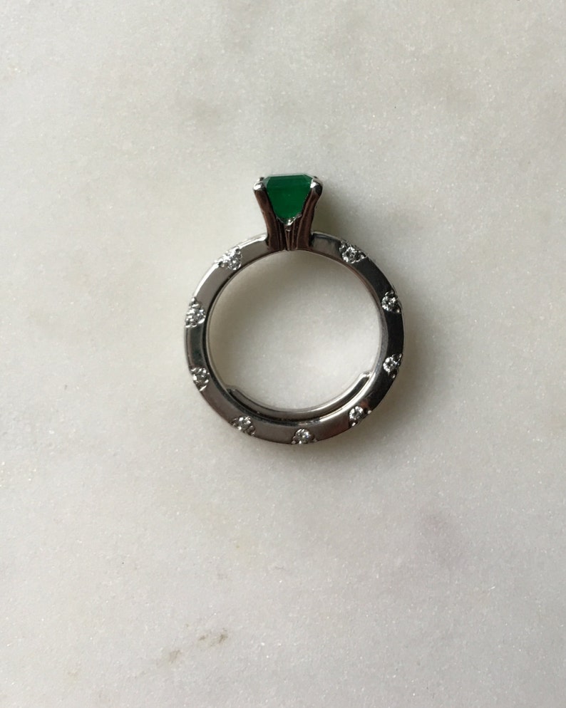 May include: A silver ring with a green gemstone and small diamonds around the band.