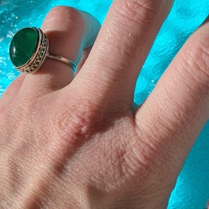 May include: A gold ring with a large oval green gemstone set in a decorative filigree design.
