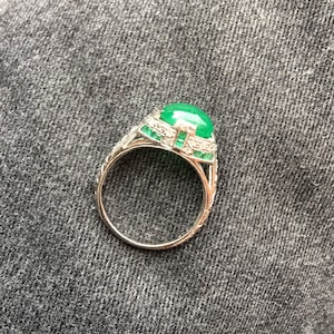 May include: A silver ring with a large green gemstone surrounded by smaller diamonds and emeralds.