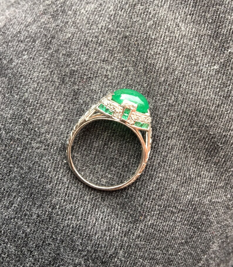 May include: A silver ring with a large green gemstone surrounded by smaller diamonds and emeralds.