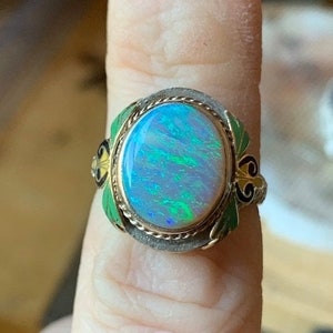 May include: A silver ring with a large oval opal gemstone set in a gold bezel. The ring is decorated with green and yellow enamel.