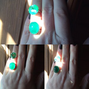 May include: Two emerald green gemstone rings with silver settings. The rings are on a person's hand.