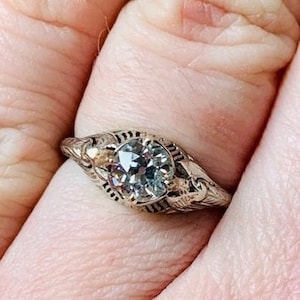 May include: A silver ring with a large, clear, round gemstone set in a filigree design. The ring has a delicate, vintage style.