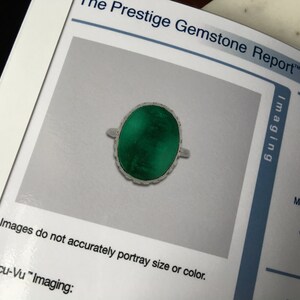May include: A green gemstone ring with a silver setting. The ring is oval shaped and has a detailed design around the edge of the stone. The ring is photographed on a white background.