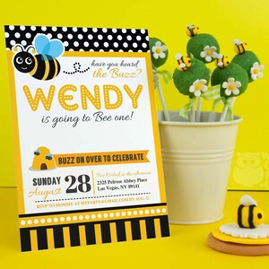 May include: A yellow and black bee-themed invitation for a first birthday party. The invitation says "have you heard the buzz? Wendy is going to bee one!" and includes details for the party, including the date, time, and location. The invitation is decorated with a cute cartoon bee.