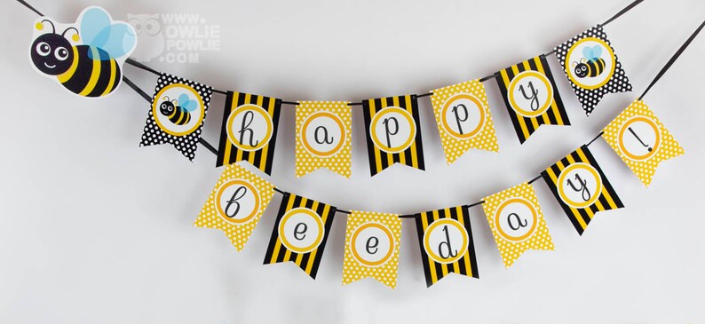May include: A yellow and black bee-themed banner with the words "happy birthday!" in gold circles. The banner is strung with black string and has a bee illustration at the top.