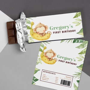 May include: A printable chocolate bar wrapper featuring a cartoon monkey sitting on a banana. The wrapper is decorated with green leaves and the text "Gregory's First Birthday".