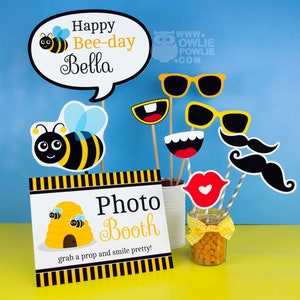 May include: A photo booth sign with a beehive and the text "Photo Booth" and "grab a prop and smile pretty!"  There are bee-themed props, including a bee, sunglasses, a mustache, and a mouth.