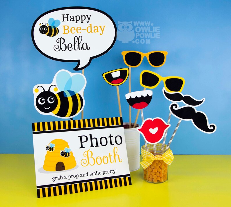 May include: A photo booth sign with a beehive and the text "Photo Booth" and "grab a prop and smile pretty!"  There are bee-themed props, including a bee, sunglasses, a mustache, and a mouth.
